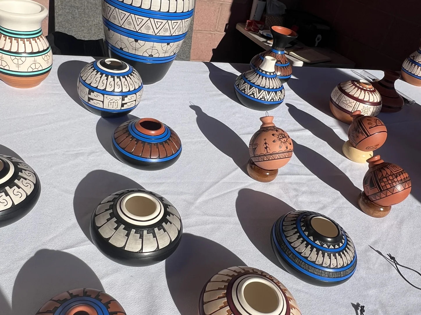 Hand-painted Navajo and Hopi pottery laid out in rows on a white cloth on a vendor's table at the monument, seed pots and bowls in black, white, blue and terracotta