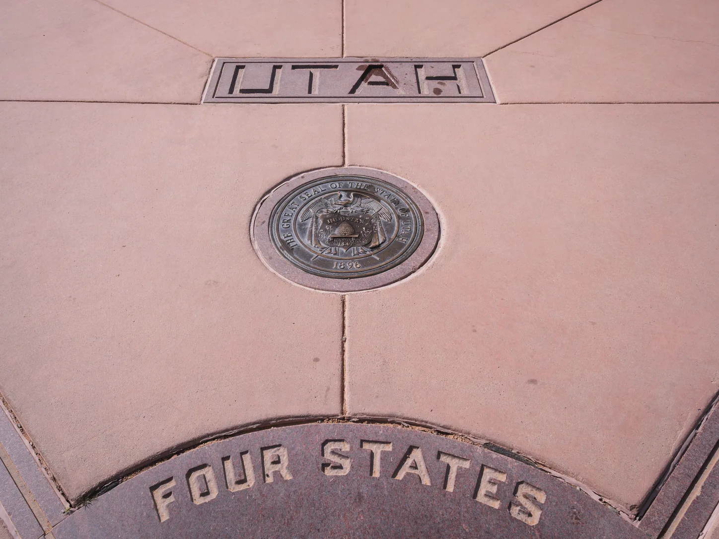 A detail of the paving on the Utah side: the word UTAH incised in the stone above the bronze Great Seal of the State of Utah, and below it the words FOUR STATES carved into the segment of the central disc