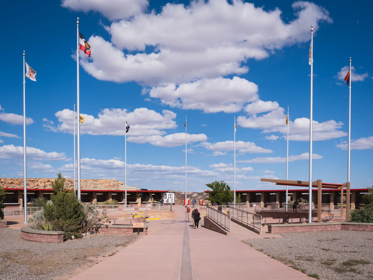 The plaza from the southern walkway, a line of flagpoles down each side and the two long open-fronted galleries that house the Navajo and Ute craft stalls, with flat desert running out behind them